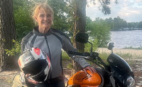 biker woman holding helmet next to motorcycle